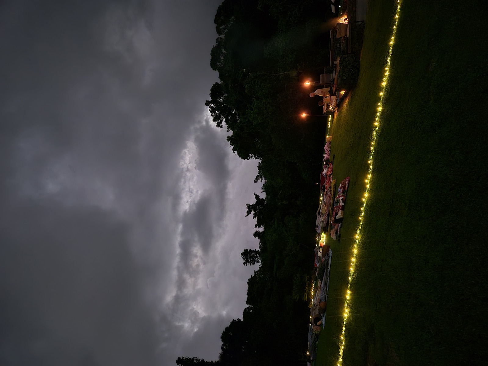 Storm clouds gather over the fairy-lit lawn at dusk