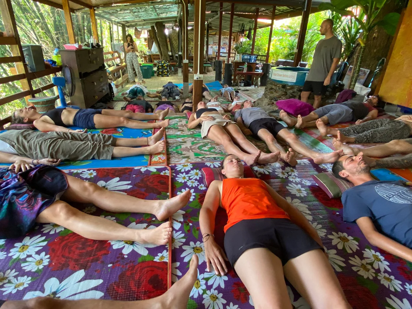 A group breathwork session, participants lying on mats in an open-sided hall.